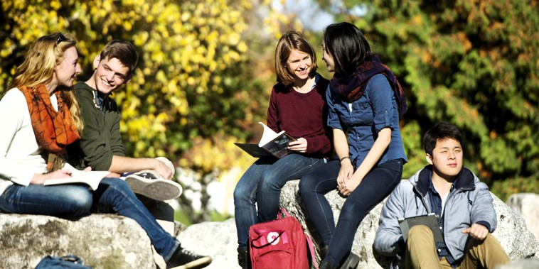 Studerende med bøger og skoletasker hygger sig i det fri