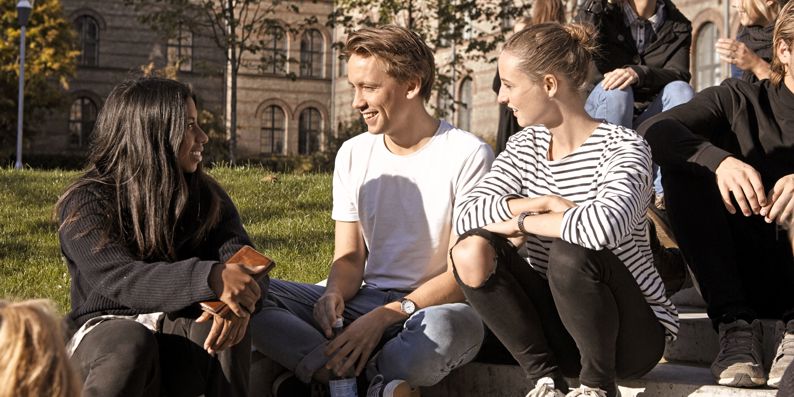 Studerende fra KU sidder på græsset foran campus