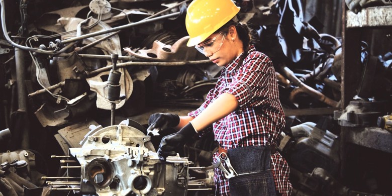 Kvinde med gul hjelm arbejder ved produktionsmaskine