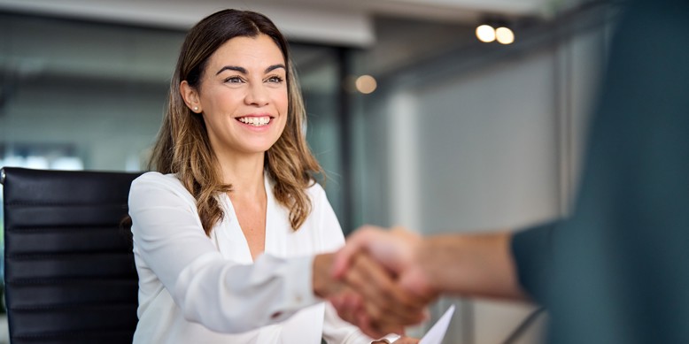 Smilende kvinde giver håndtryk til en anonym person