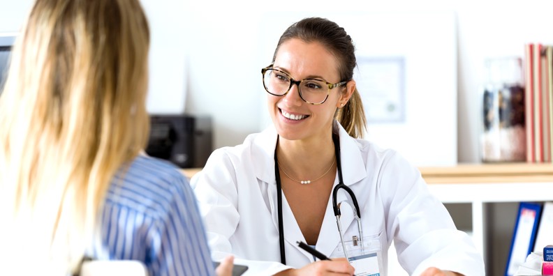 Smilende kvindelig læge taler med kvindelig patient