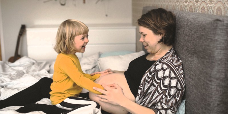 Gravid mor med grinende datter på skødet