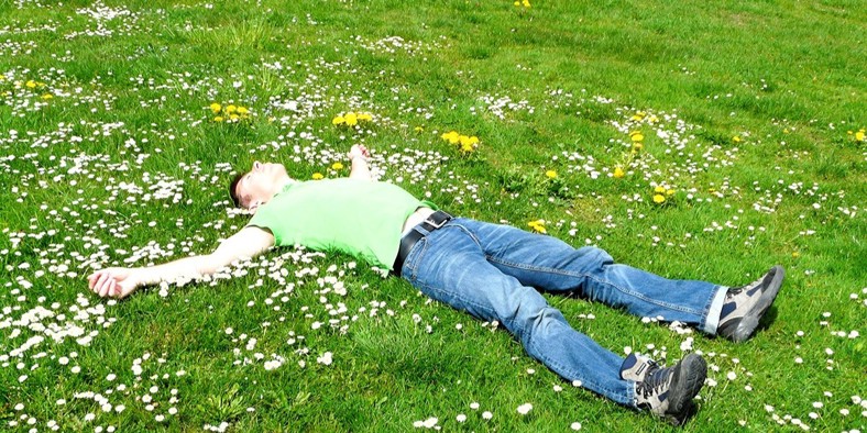 Mand ligger udstrakt på græsplæne med armene ud til siden